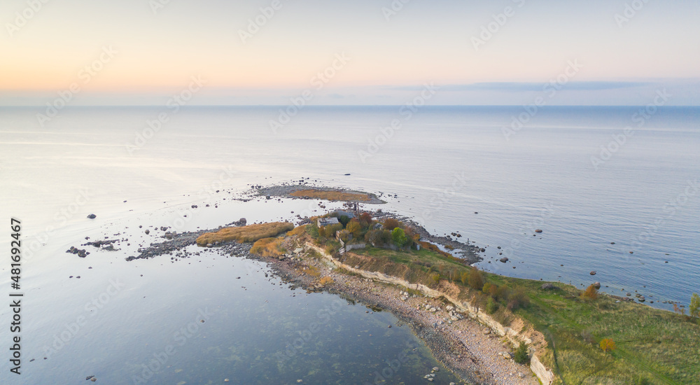 Aerial sunset colored view to the thin cape badly suffering by coastal erosion and with the abandoned historic guard station buildings, nearly to collapse to the sea. Concept of coastal erosion