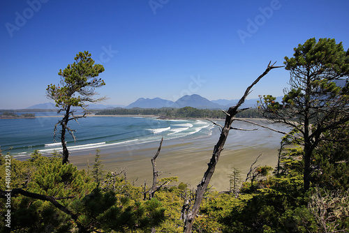 Aerial view of Cox Bay beach in Tofino with ocean waves and mountains in background during low tide. © Jara