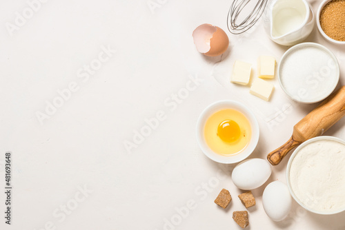 Baking ingredients at white table. Flour, brown sugar, milk, eggs and utensils. Top view with copy space.