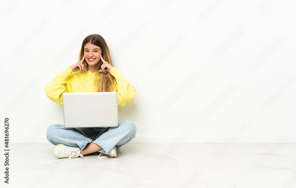 Fototapeta premium Young woman with a laptop sitting on the floor smiling with a happy and pleasant expression
