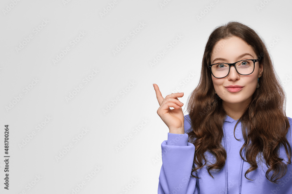 A smiling teenage girl with long hair and glasses. The girl is wearing a violet oversized sweatshirt, pointing up. A smiling teenage girl with long hair and glasses. The girl is wearing a violet oversized sweatshirt, pointing up.