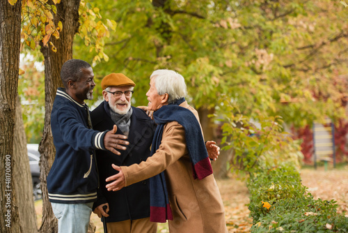 Positive multiethnic men hugging in autumn park.
