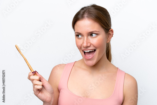 Young caucasian woman isolated on white background with a toothbrush and surprised expression