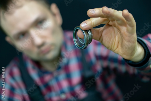 A young guy holds a bearing in his hand on a black background. A bicycle mechanic in the workshop changes bearings for the steering column. Repair of motorcycles and cars in the service center.