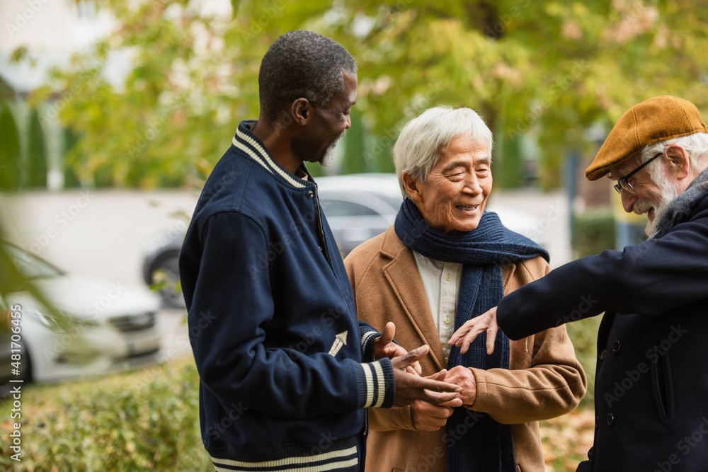 Happy senior man talking to multicultural friends in autumn park.