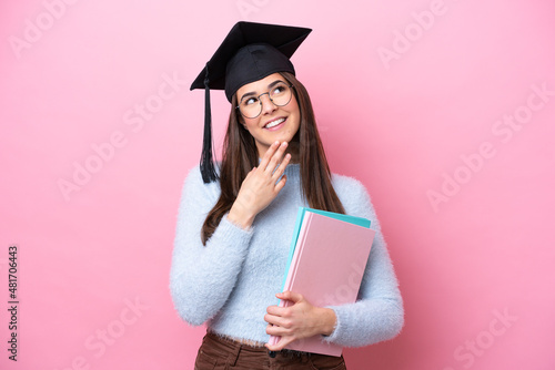 Young student Brazilian woman wearing graduated hat isolated on pink background looking up while smiling