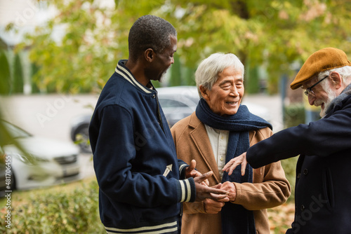 Happy senior man talking to multicultural friends in autumn park.