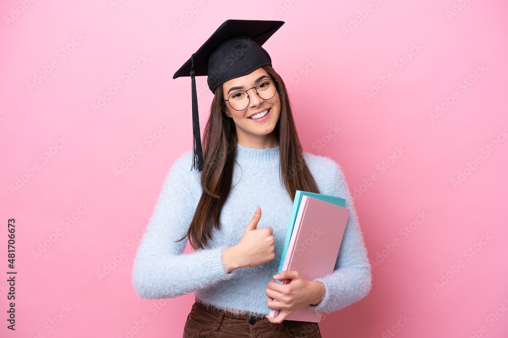 Young student Brazilian woman wearing graduated hat isolated on pink background giving a thumbs up gesture Young student Brazilian woman wearing graduated hat isolated on pink background giving a thumbs up gesture