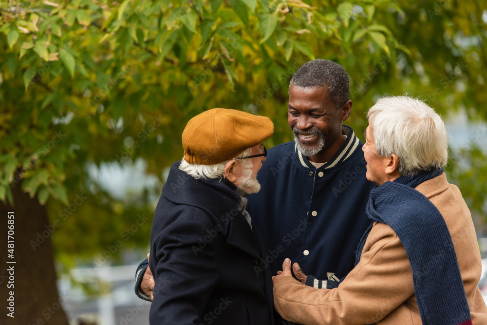 Fototapeta premium Positive multiethnic men hugging in autumn park.