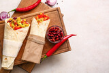 Board with delicious burritos and ingredients on light background