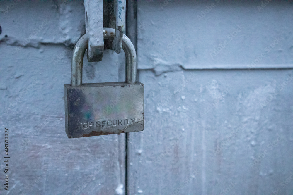 A metal lock with engraved text Top Secret hangs on the blue garage door. Protection of the house or other property from burglars, thieves. Private territory. Locked up door from outdoors. A padlock. A metal lock with engraved text Top Secret hangs on the blue garage door. Protection of the house or other property from burglars, thieves. Private territory. Locked up door from outdoors. A padlock.