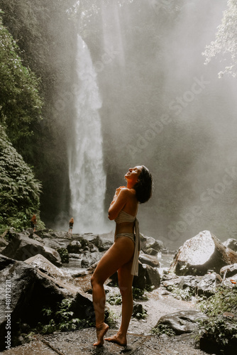 A young woman traveller is exploring a waterfall in tropical settings of Bali islands  Indonesia. Tropical forest  lush greenery  river