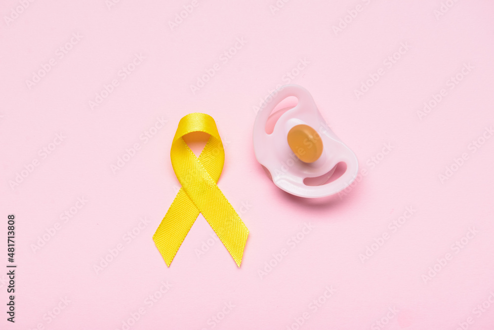Golden awareness ribbon and pacifier on color background. International Childhood Cancer Day