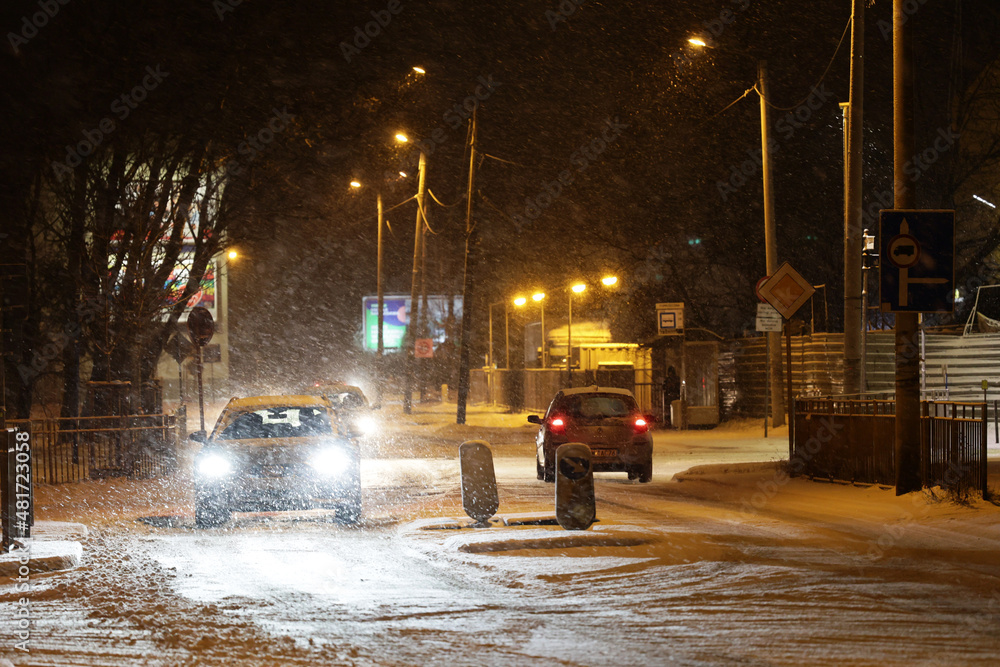 Pojazdy pług i piaskarka na drodze po nocnych opadach śniegu w mieście i ruch pojazdów.  - obrazy, fototapety, plakaty 