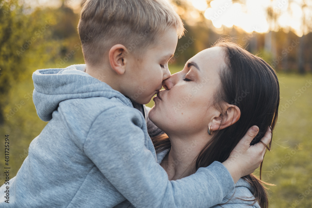 Close-up portrait of a boy kissing mother standing outdoors. Outdoor portrait. Family care. Close-up portrait of a boy kissing mother standing outdoors. Outdoor portrait. Family care.