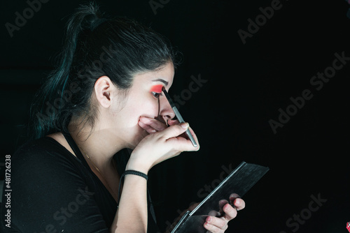 beautiful latina woman with green hair, making up her eyes with a red eye shadow. girl holding her brush while putting it on her right eye. black background. beauty concept. photo