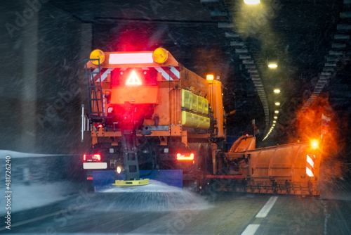 Winter service vehicle in work drives into a tunnel. Image blurred due to snow and salt