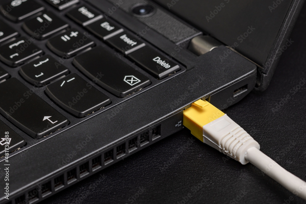 Computer ethernet network cable with yellow RJ-45 connector inserted into the black laptop on black background Computer ethernet network cable with yellow RJ-45 connector inserted into the black laptop on black background