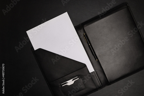 Black leather file folder agenda organizer opened with white blank paper sheet and pen on black background with copy space photo
