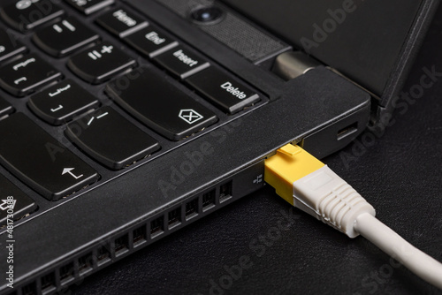 Computer ethernet network cable with yellow RJ-45 connector inserted into the black laptop on black background