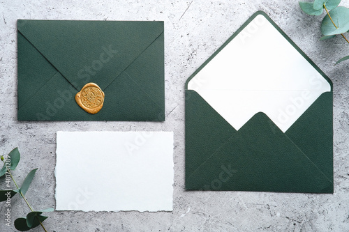 Wedding stationery set. Green envelopes and blank paper card on concrete table with eucalyptus branches.