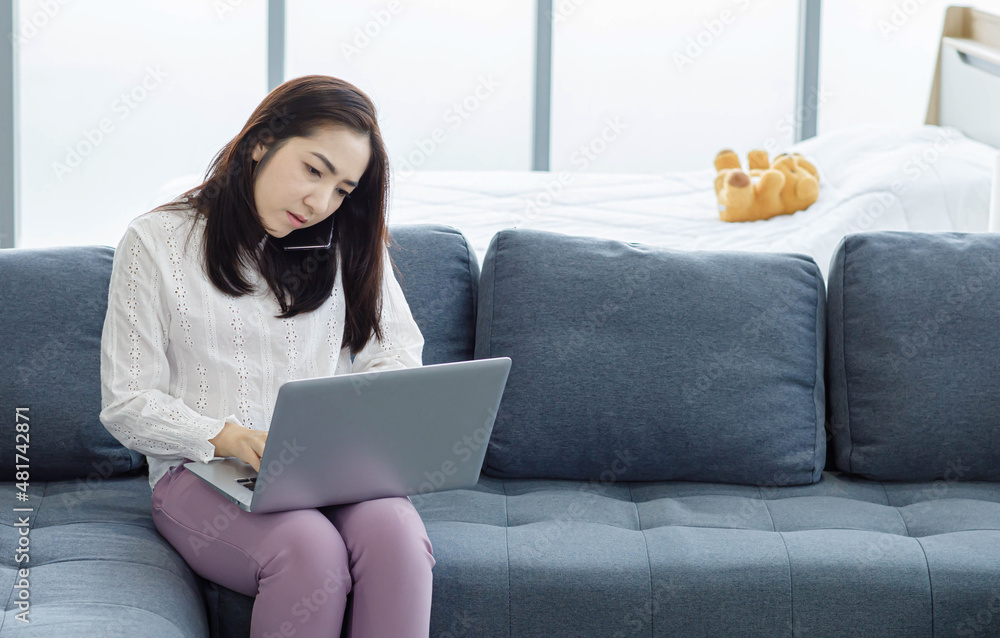 Naklejka premium Portrait of Asian young female long hair freelancer sitting on cozy sofa use laptop computer working from home.