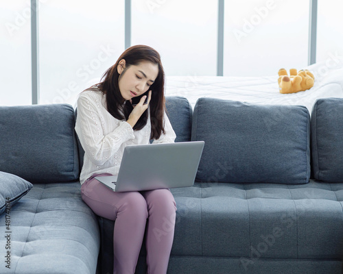 Portrait of Asian young female long hair freelancer sitting on cozy sofa use laptop computer working from home.