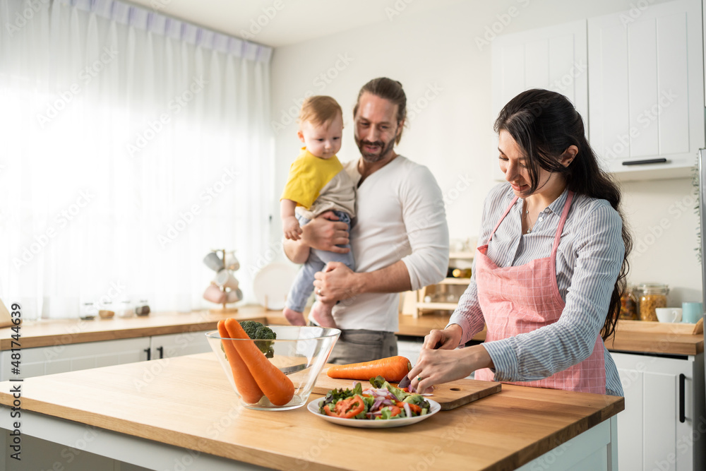 Caucasian beautiful parents cook food with baby boy toddler in kitchen. Caucasian beautiful parents cook food with baby boy toddler in kitchen.