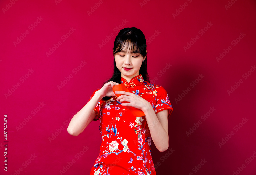 Beautiful Asian girl in traditional cheongsam on red background holding red envelope. Beautiful Asian girl in traditional cheongsam on red background holding red envelope.
