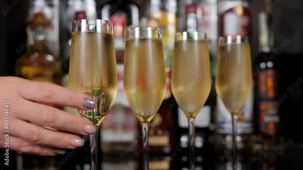 Close-up of a woman taking a glass of cold champagne in a bar. A row of champagne glasses on the bar. Close-up of a woman taking a glass of cold champagne in a bar. A row of champagne glasses on the bar.