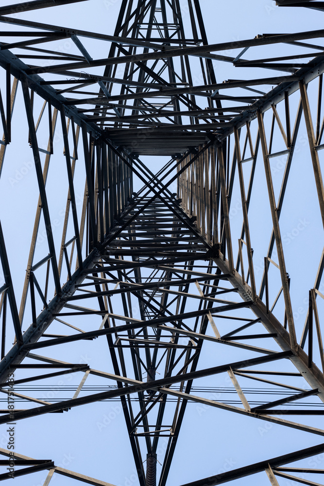 Close up bottom view of high voltage electricity transmission tower under the clean blue sky