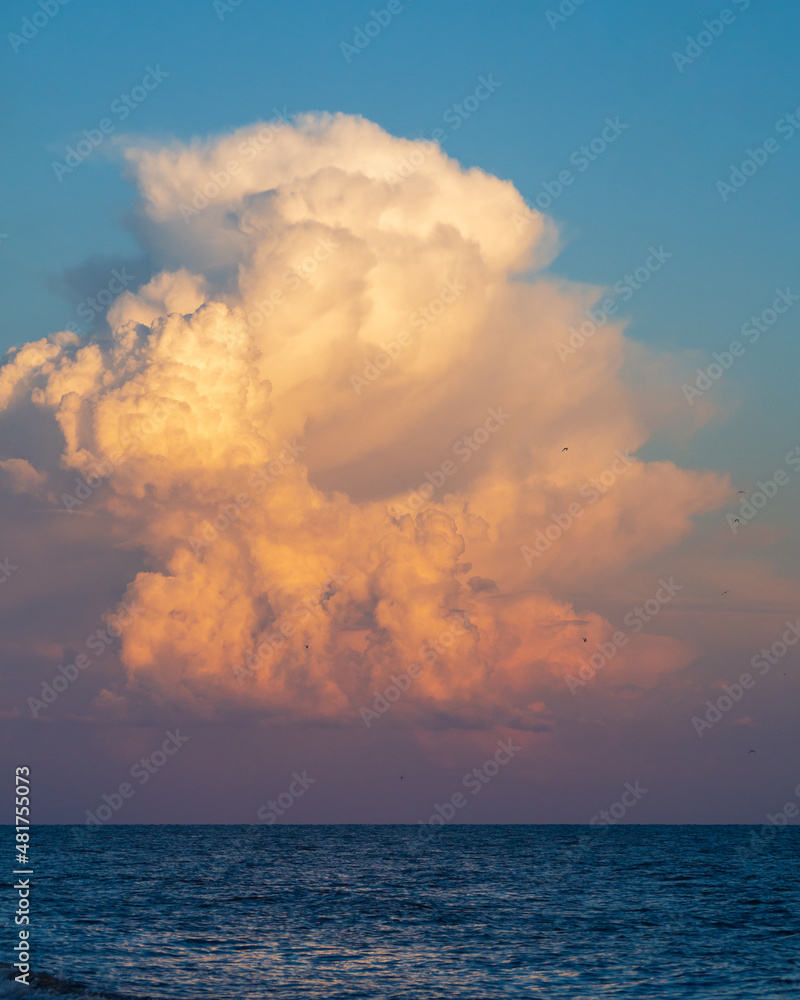 Sky background over the sea. A huge funnel-shaped cloud in the sunset light. An original beautiful cloud over the water