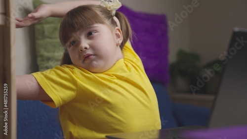 Tired little girl stretches arms body at break at home class