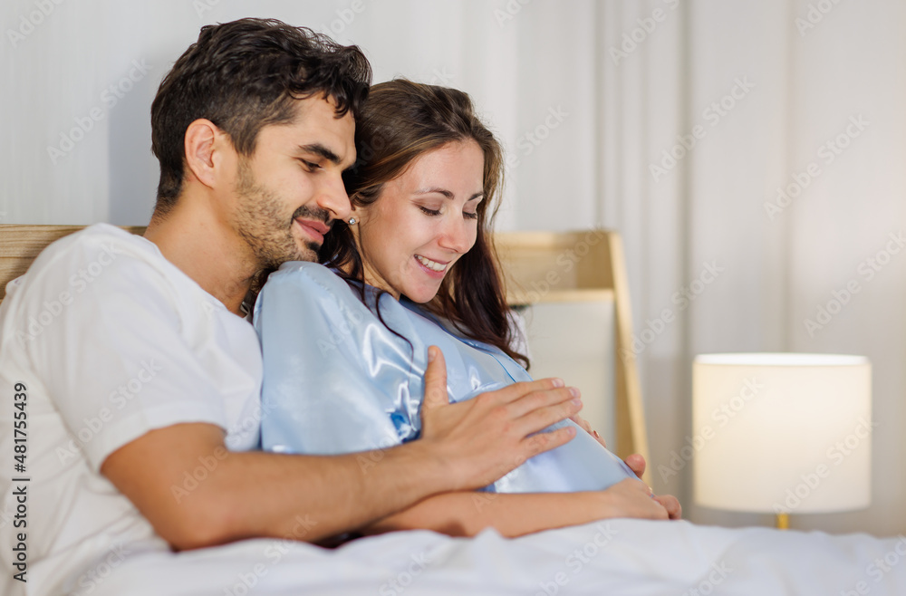 Cheerful husband enjoy embracing pregnant wife and happy to tenderly fondle beloved belly of unborn baby and expecting warm family during prenatal care of maternity at romantic bedroom Cheerful husband enjoy embracing pregnant wife and happy to tenderly fondle beloved belly of unborn baby and expecting warm family during prenatal care of maternity at romantic bedroom