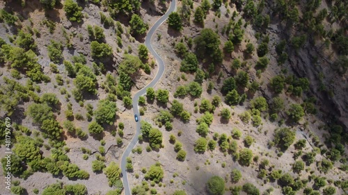 Passenger car along a winding road in an arid landscape with green trees and bushes, Heirro, Spain - aerial view from a drone photo