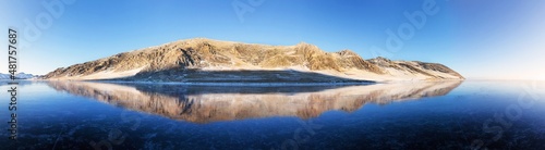 Panoramic view from blue ice to snowy coastal hills in sunny cold day. Beautiful winter landscape of frozen Baikal Lake. Natural background, banner, space for text at bottom. Ice travel concept