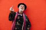 Mature man showing his middle finger while standing against a red background