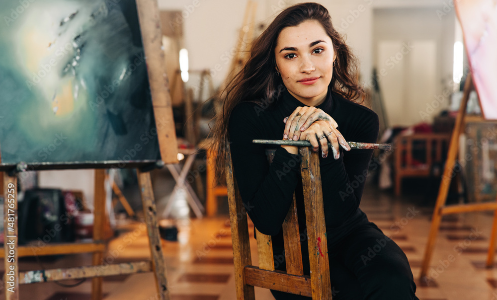 Young female artist looking at the camera while sitting in her art workshop Young female artist looking at the camera while sitting in her art workshop