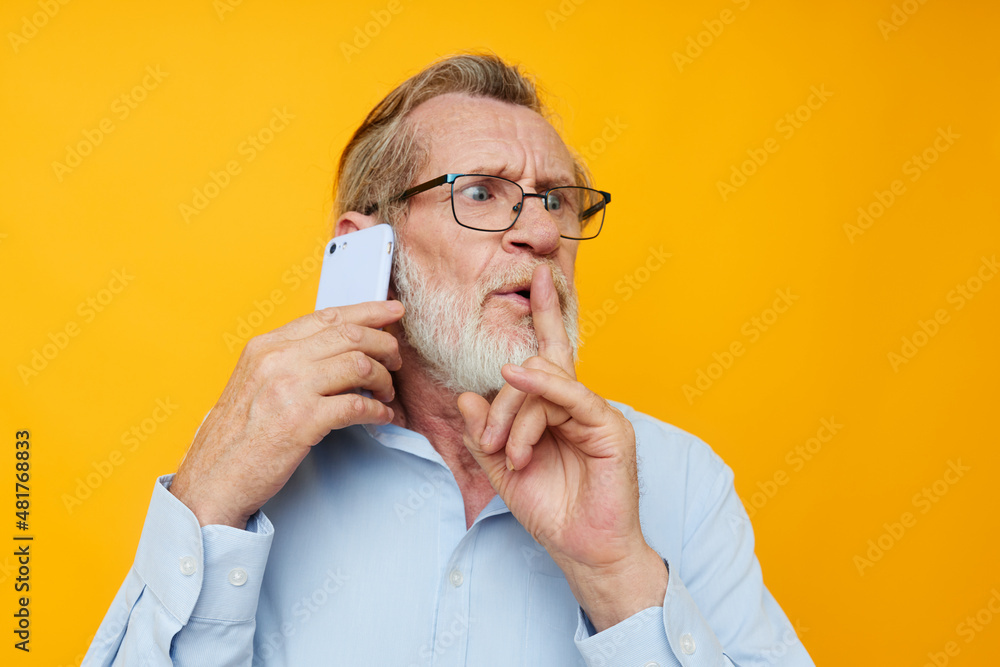 Portrait elderly man in a blue shirt and glasses talking on the phone unaltered Portrait elderly man in a blue shirt and glasses talking on the phone unaltered
