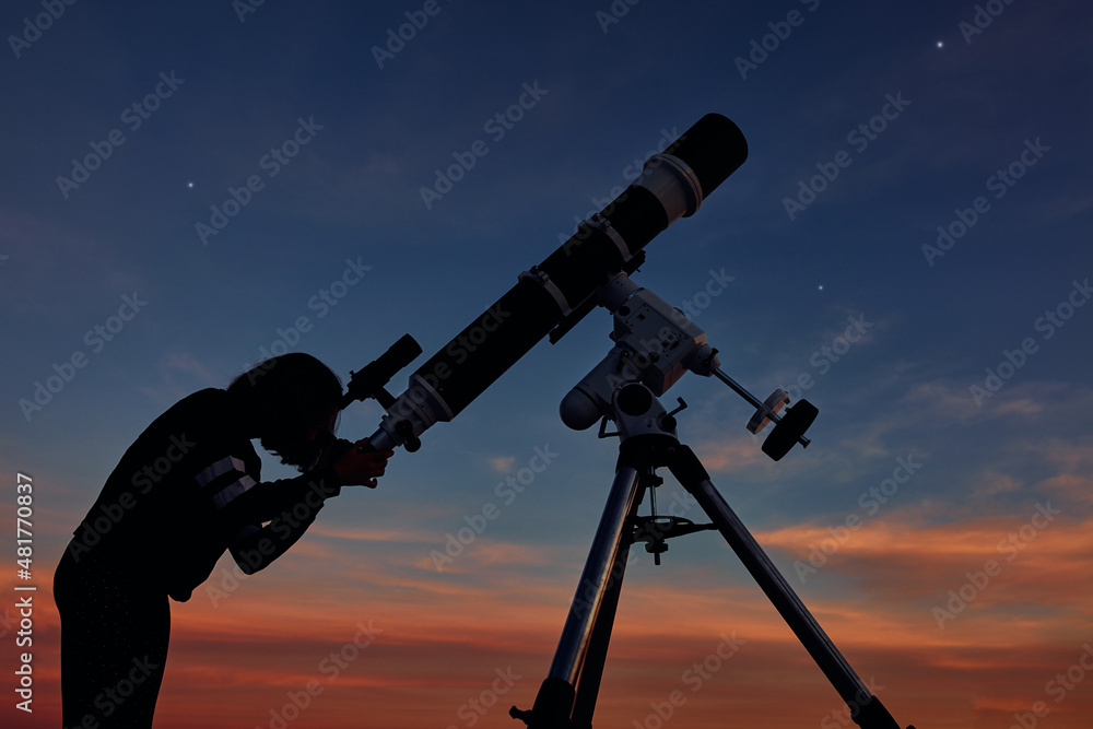 Girl with astronomical telescope stargazing under twilight sky.