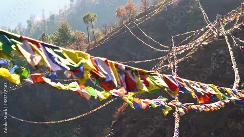 Slow motion shot of colorful Buddhist Tibetan prayer flag in front of mountains at Pangan Nyingmapa Monastery in Patlikuhal village near Manali, Himachal Pradesh, India	