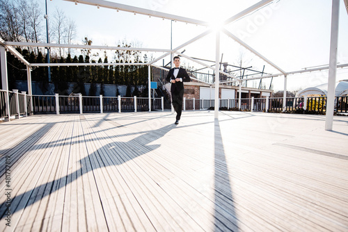 Caucasian groom in black suit walking on wooden terrace