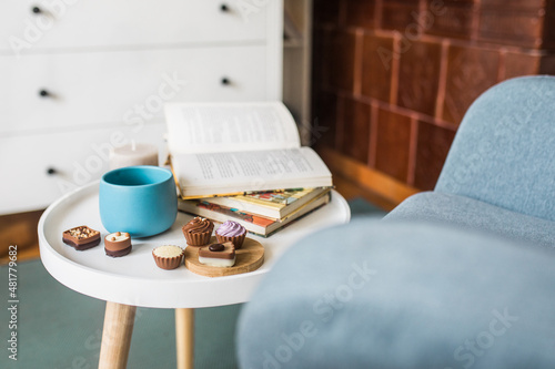Side view photo of book  cup of green tea and chocolate pralines on round white side table  Scandinavian design  copy space