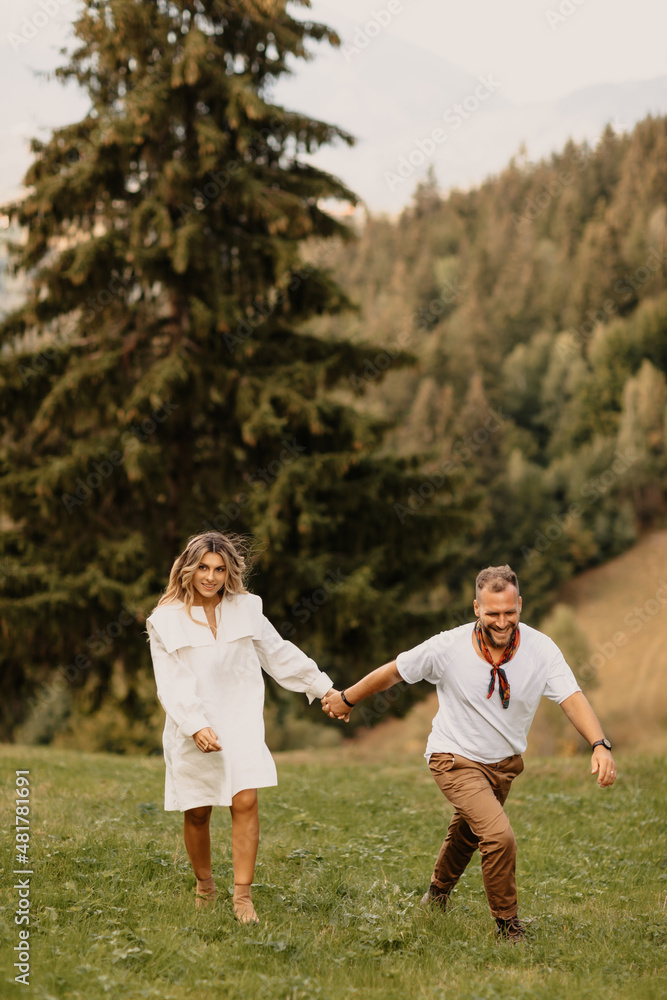 Outdoor shot of young couple in love walking on through grass field in the mountain area Outdoor shot of young couple in love walking on through grass field in the mountain area