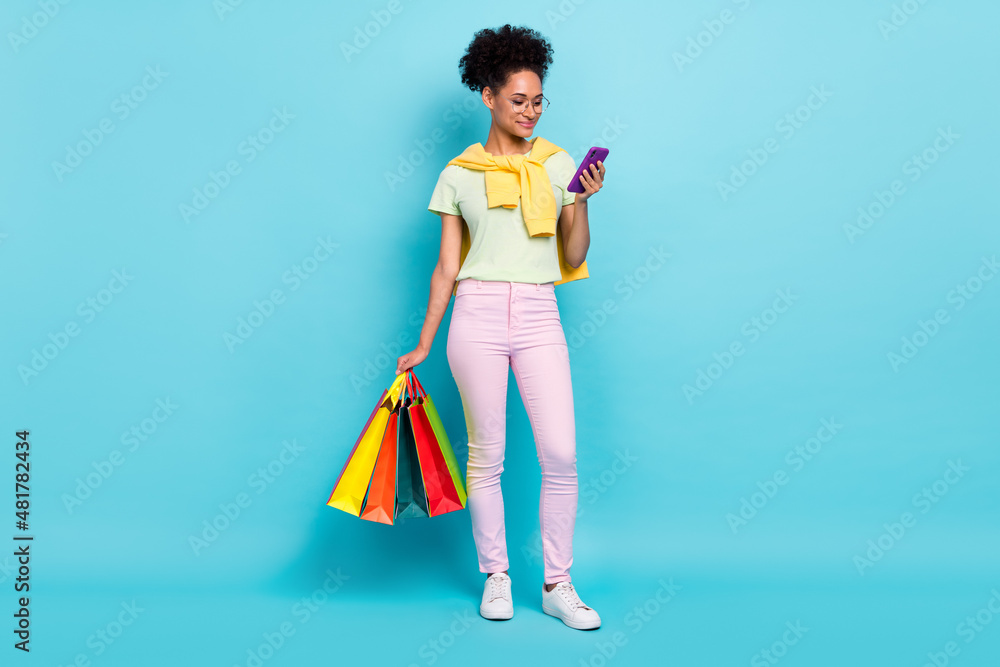 Full length photo of young african girl use mobile shopping store mall holiday purchase present isolated over blue color background Full length photo of young african girl use mobile shopping store mall holiday purchase present isolated over blue color background