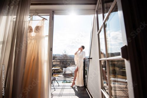 Bride in robe and high heels posing on balcony of hotel room