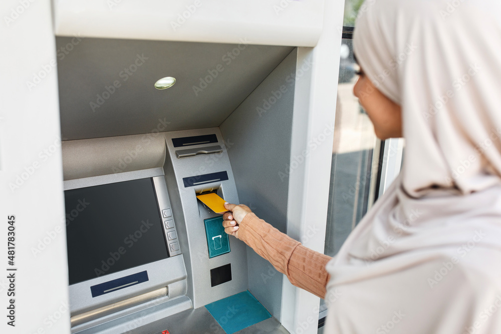 Currency, finance and transactions. Lady inserting an bank credit card into ATM machine to transfer money outdoor Currency, finance and transactions. Lady inserting an bank credit card into ATM machine to transfer money outdoor