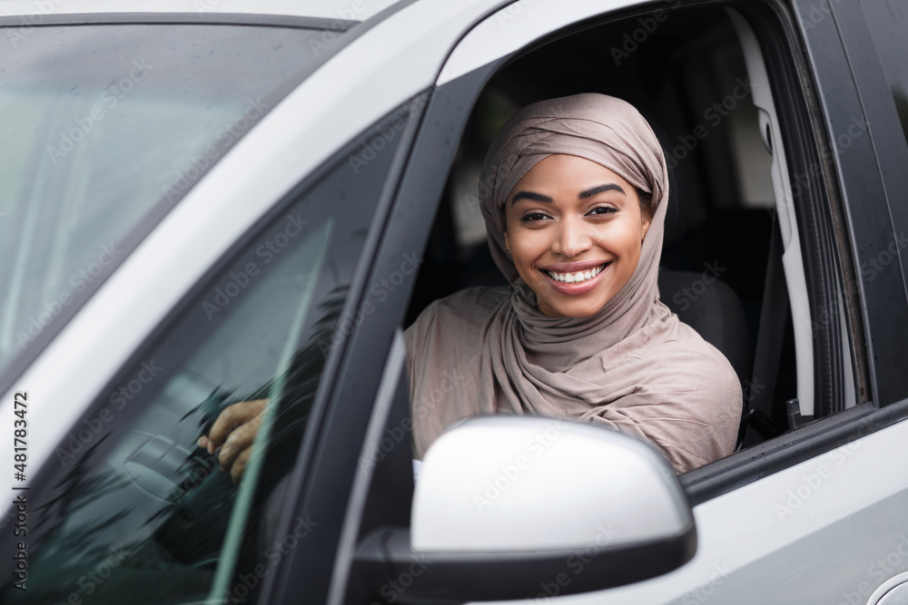 Cheerful islamic african american lady driver in hijab sits in new car at steering wheel and look at camera Cheerful islamic african american lady driver in hijab sits in new car at steering wheel and look at camera