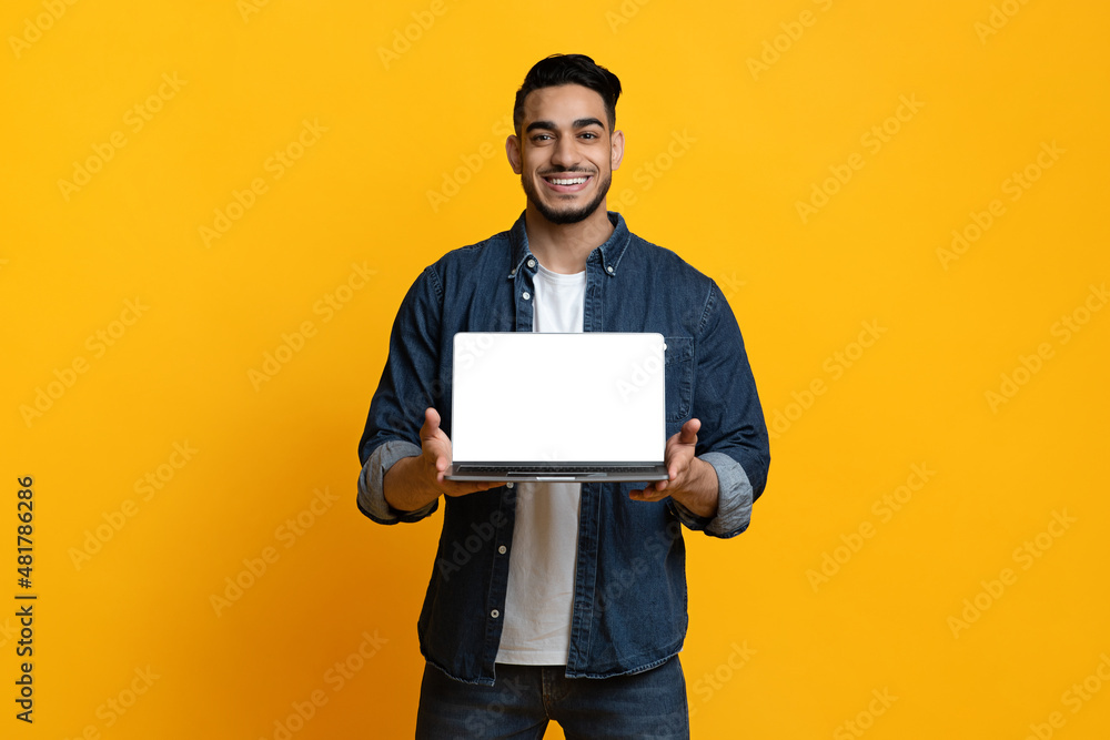Cheerful arab guy showing laptop with blank screen
