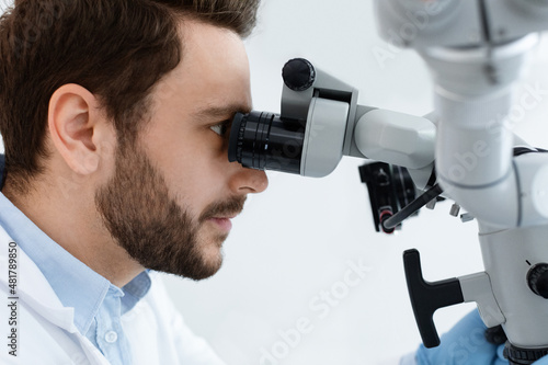 Bearded man stomatologist looking at dental microscope